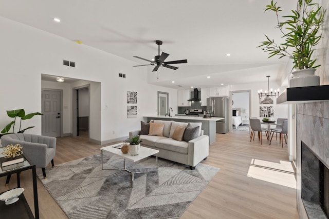 living room featuring light hardwood / wood-style floors, ceiling fan with notable chandelier, a fireplace, lofted ceiling, and sink