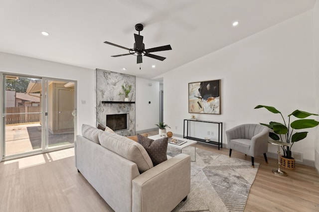 living room with light hardwood / wood-style flooring, a high end fireplace, ceiling fan, and vaulted ceiling