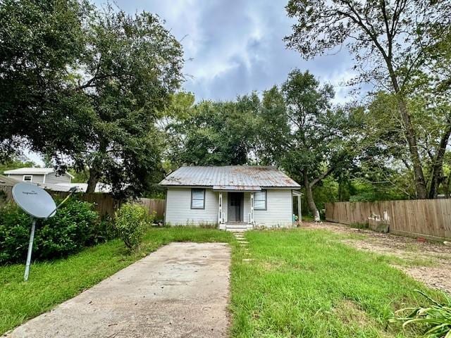 view of front facade featuring fence, driveway, a front lawn, and metal roof
