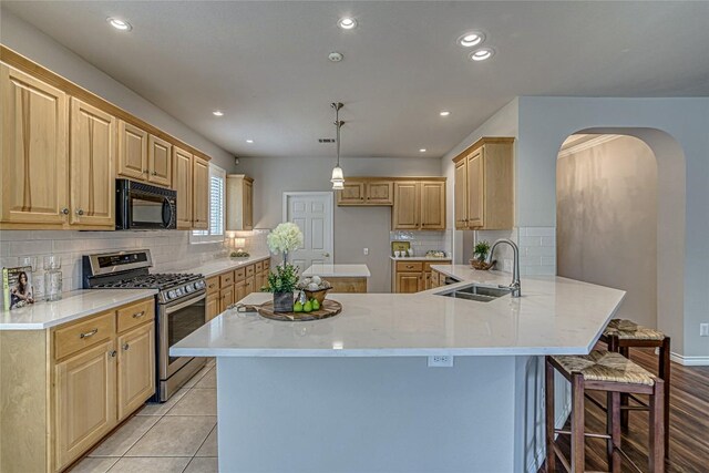 kitchen with sink, kitchen peninsula, light brown cabinets, a breakfast bar area, and stainless steel gas stove