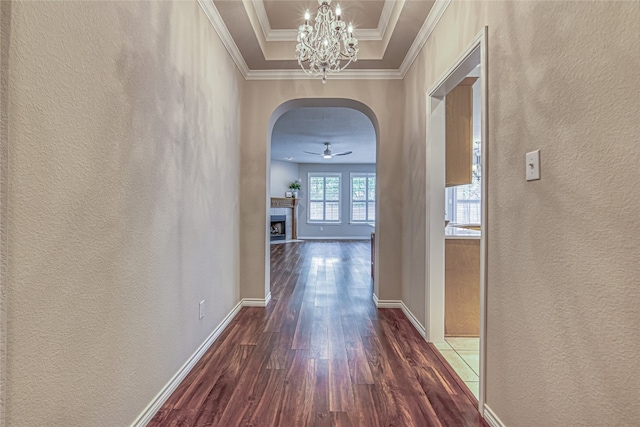 corridor with ornamental molding, dark hardwood / wood-style flooring, a raised ceiling, and a notable chandelier