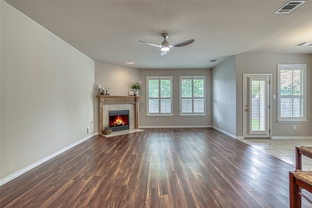 unfurnished living room with a tiled fireplace, dark wood-type flooring, and ceiling fan