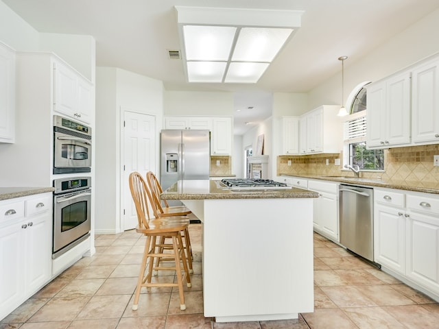 kitchen featuring appliances with stainless steel finishes, light stone counters, a center island, and white cabinets