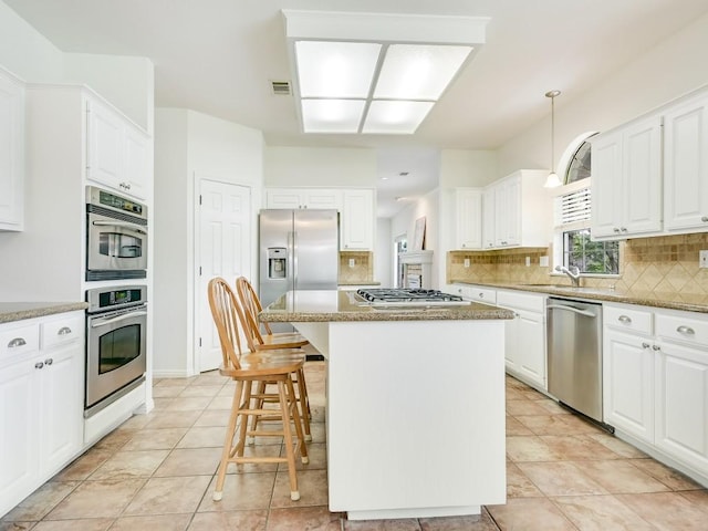 3503 Misty Creek Dr, Austin, TX 78735 - kitchen with stainless steel appliances, backsplash, a kitchen island, white cabinets, and a kitchen breakfast bar