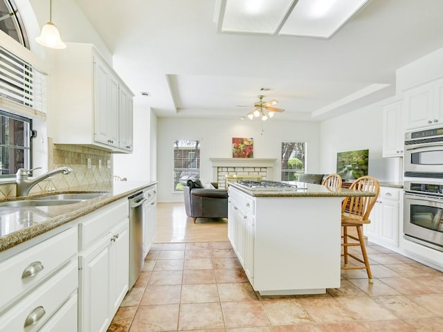 kitchen with tasteful backsplash, appliances with stainless steel finishes, a fireplace, a raised ceiling, and a sink