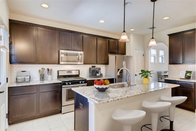 kitchen with a kitchen island with sink, sink, stainless steel appliances, and light stone counters