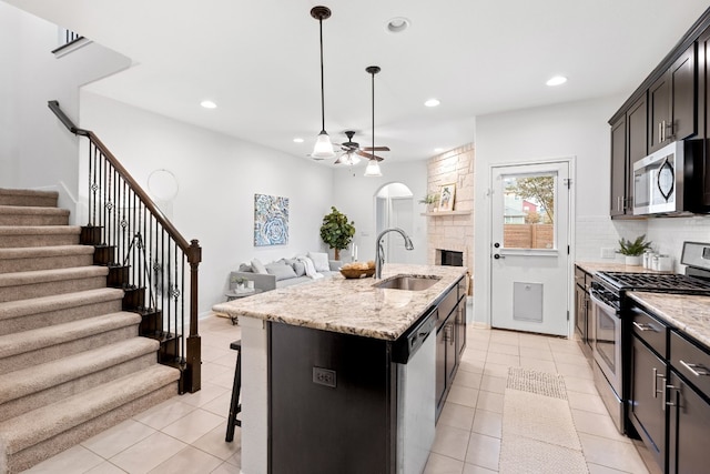 kitchen featuring light stone countertops, sink, an island with sink, decorative light fixtures, and appliances with stainless steel finishes