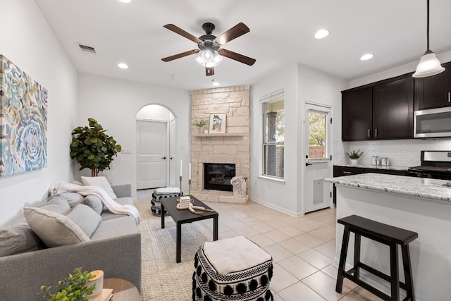 living room featuring ceiling fan, a stone fireplace, and light tile patterned floors