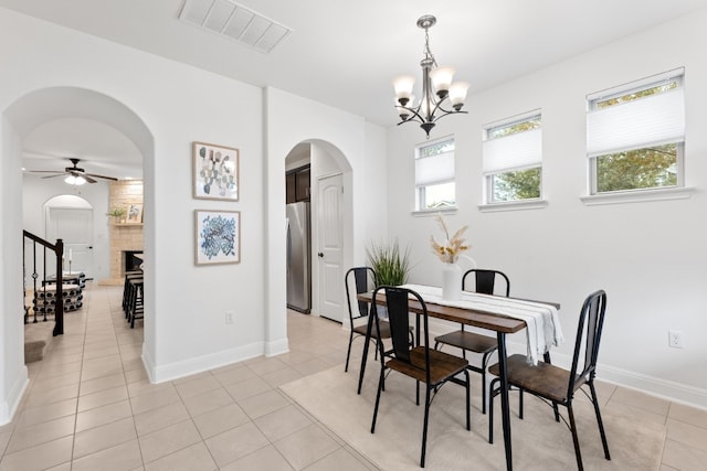 dining space featuring light tile patterned floors, ceiling fan with notable chandelier, and a large fireplace