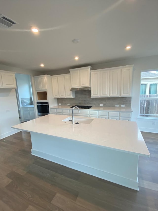 kitchen with white cabinets, oven, a large island, and sink