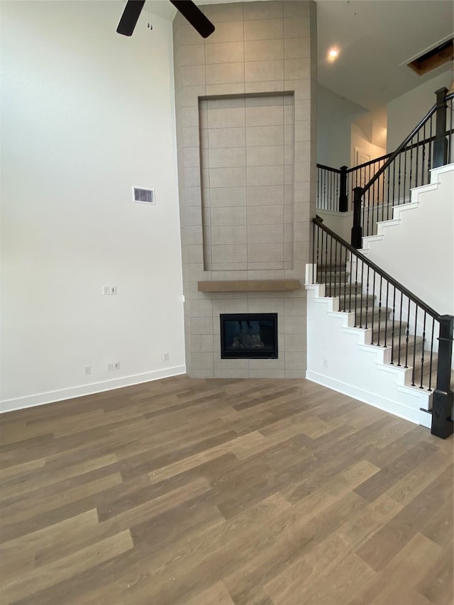 unfurnished living room with a tiled fireplace, hardwood / wood-style floors, a high ceiling, and ceiling fan