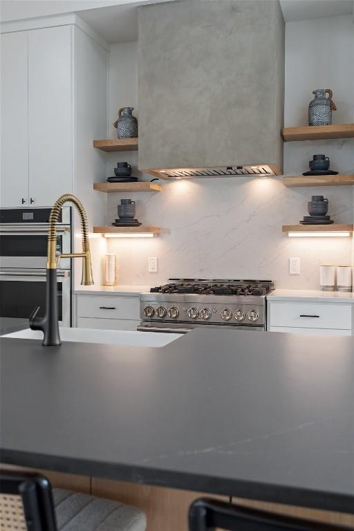 kitchen with wall chimney exhaust hood, white cabinetry, stainless steel range, and backsplash