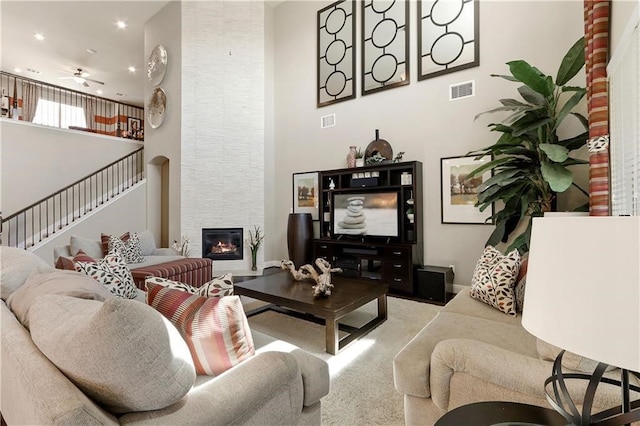 living room with light carpet, a high ceiling, ceiling fan, and a large fireplace