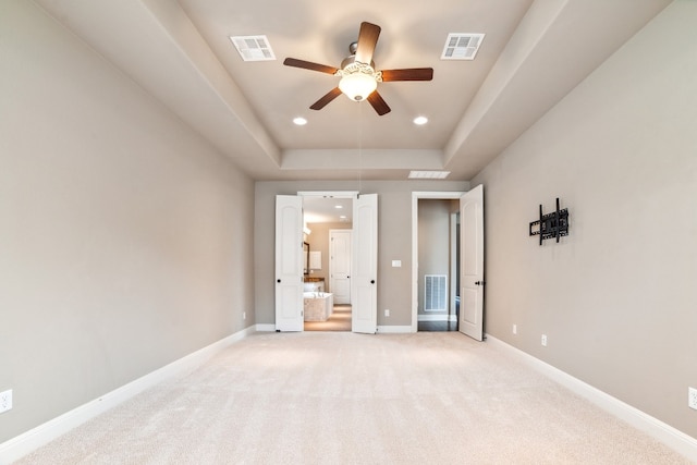 unfurnished bedroom with light carpet, ceiling fan, and a raised ceiling