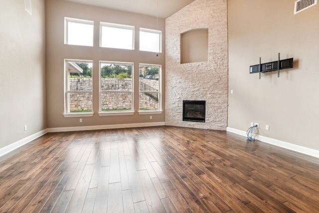 unfurnished living room featuring a stone fireplace, dark wood-type flooring, and a high ceiling