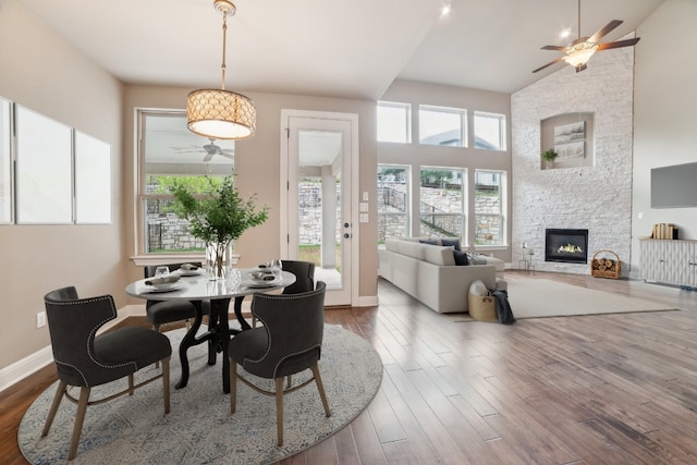 dining space featuring a fireplace, high vaulted ceiling, hardwood / wood-style flooring, and ceiling fan