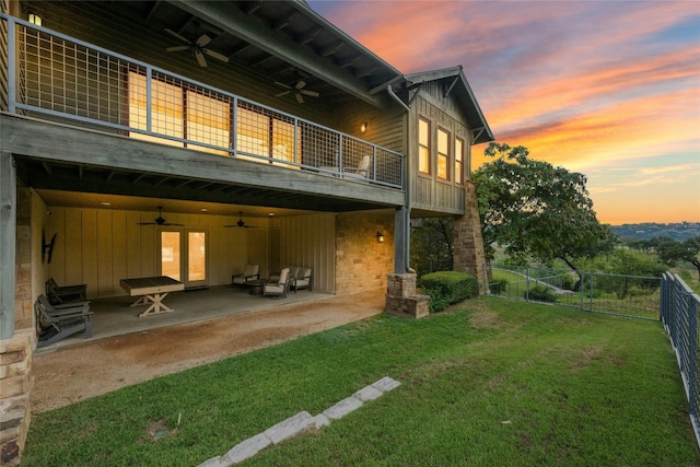 back house at dusk featuring a yard, ceiling fan, a patio, and a balcony