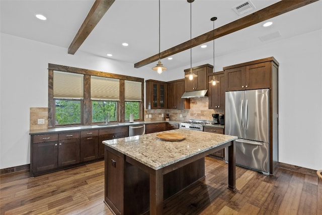 kitchen with beamed ceiling, stainless steel appliances, dark hardwood / wood-style flooring, a kitchen island, and light stone countertops