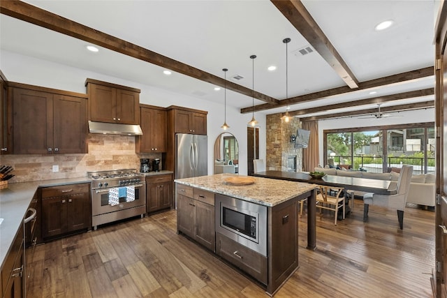 kitchen with decorative light fixtures, stainless steel appliances, a center island, light stone countertops, and dark hardwood / wood-style floors