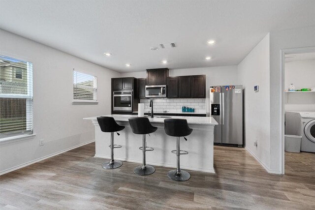 kitchen with a kitchen bar, washer / dryer, dark brown cabinets, an island with sink, and stainless steel appliances