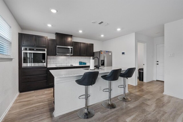 kitchen with sink, light hardwood / wood-style flooring, a breakfast bar area, stainless steel appliances, and an island with sink