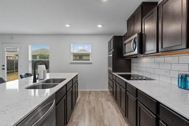 kitchen featuring sink, appliances with stainless steel finishes, tasteful backsplash, light stone counters, and light wood-type flooring