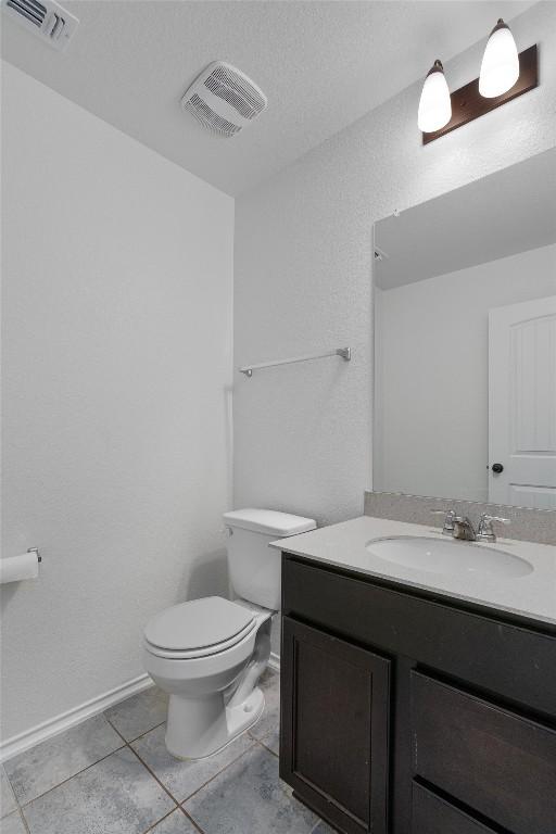 half bath with vanity, toilet, visible vents, and tile patterned flooring