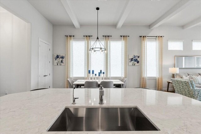 kitchen with beamed ceiling, a chandelier, light stone counters, and decorative light fixtures