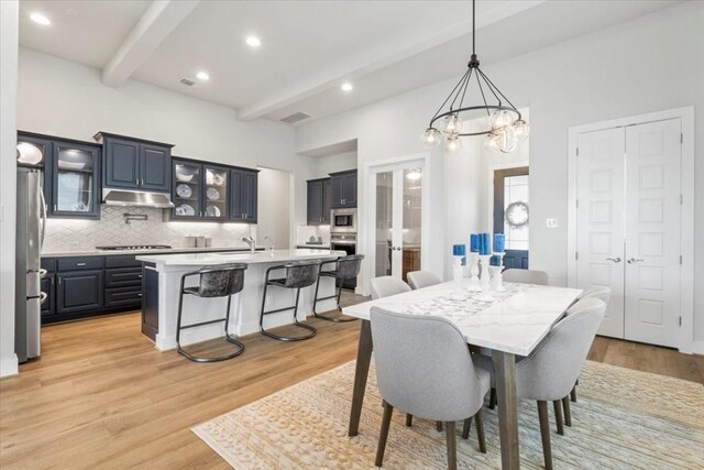 dining area featuring sink, a notable chandelier, beamed ceiling, and light hardwood / wood-style floors