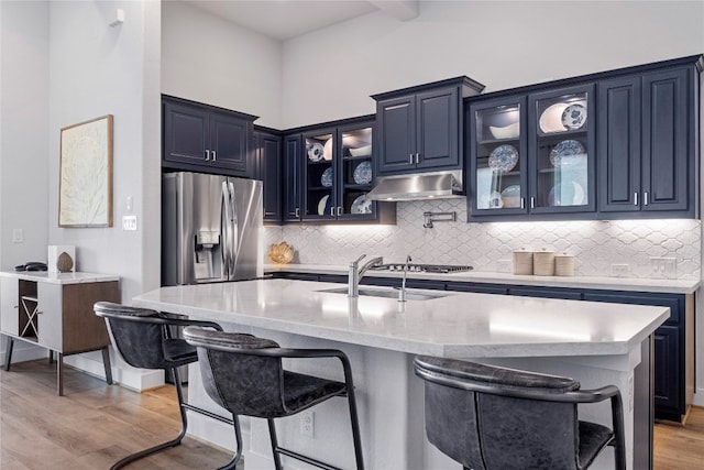 kitchen featuring a center island with sink, blue cabinets, stainless steel fridge with ice dispenser, a breakfast bar, and light wood-type flooring