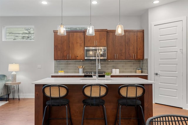 kitchen with tasteful backsplash, a kitchen island with sink, and hanging light fixtures