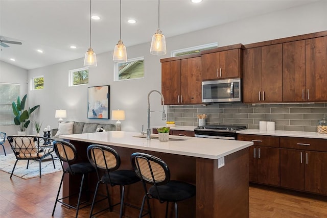 kitchen with a kitchen breakfast bar, dark hardwood / wood-style flooring, stainless steel appliances, a kitchen island with sink, and sink