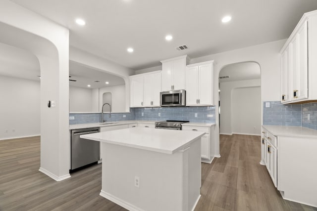 kitchen featuring white cabinetry, tasteful backsplash, stainless steel appliances, a center island, and light hardwood / wood-style floors