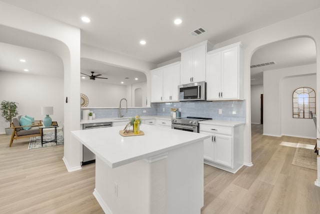 kitchen featuring light hardwood / wood-style flooring, appliances with stainless steel finishes, white cabinetry, kitchen peninsula, and ceiling fan