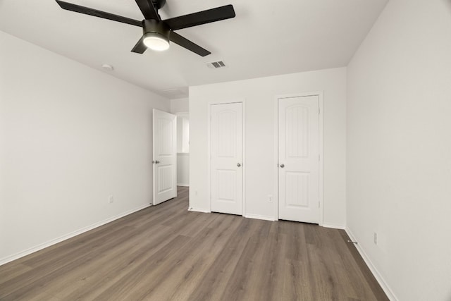 unfurnished bedroom with two closets, ceiling fan, and wood-type flooring