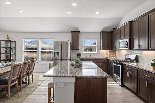 kitchen with light hardwood / wood-style flooring, vaulted ceiling, a kitchen island, light stone counters, and appliances with stainless steel finishes