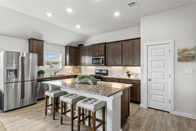 kitchen featuring vaulted ceiling, light wood-type flooring, appliances with stainless steel finishes, light stone counters, and a kitchen island