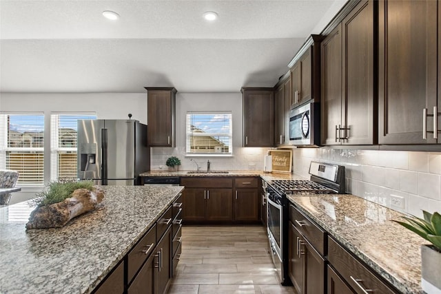 kitchen featuring a sink, dark brown cabinetry, light stone counters, and stainless steel appliances