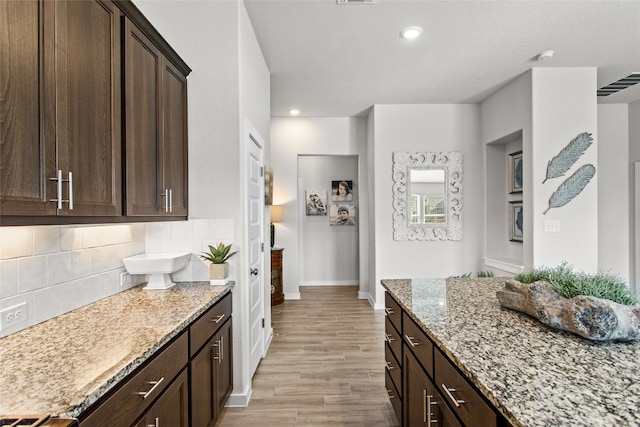 kitchen with light wood-type flooring, light stone counters, dark brown cabinetry, and tasteful backsplash