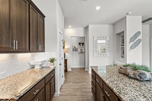 kitchen with light wood finished floors, visible vents, light stone countertops, dark brown cabinetry, and decorative backsplash