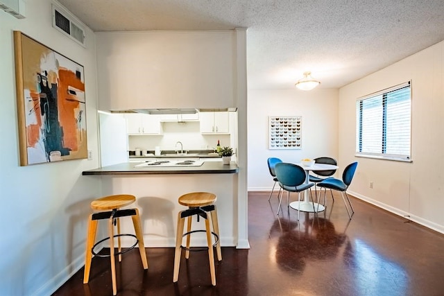 kitchen featuring white cabinets, sink, kitchen peninsula, a kitchen breakfast bar, and a textured ceiling