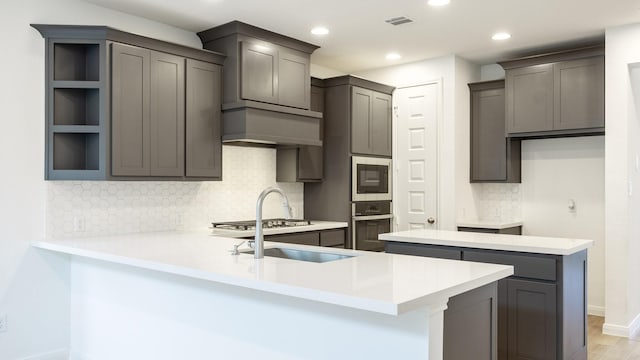 kitchen with built in microwave, sink, kitchen peninsula, oven, and light wood-type flooring