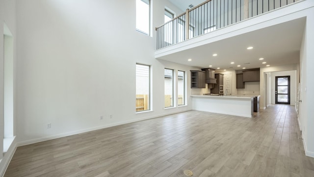 unfurnished living room featuring a high ceiling and light hardwood / wood-style flooring