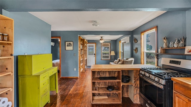 kitchen with a wall mounted AC, stainless steel range with gas stovetop, wood counters, dark hardwood / wood-style floors, and ceiling fan