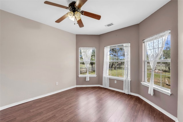 empty room featuring a wealth of natural light, ceiling fan, and dark hardwood / wood-style floors