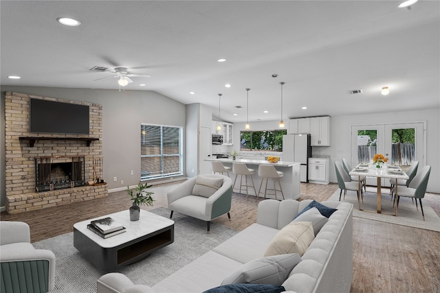 living room featuring french doors, a brick fireplace, lofted ceiling, ceiling fan, and light wood-type flooring