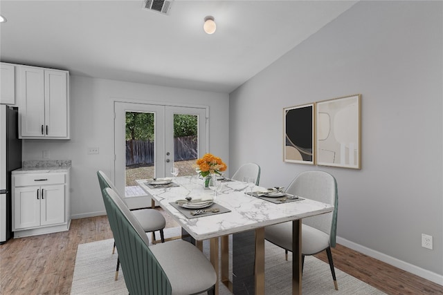 dining area featuring vaulted ceiling, french doors, and light hardwood / wood-style floors