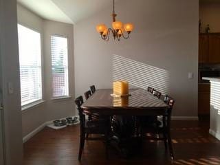 dining room featuring a wealth of natural light, dark hardwood / wood-style flooring, vaulted ceiling, and a chandelier