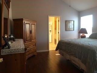 bedroom with vaulted ceiling, ensuite bathroom, and dark hardwood / wood-style floors