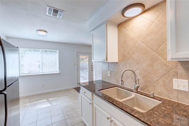 kitchen with stainless steel refrigerator, sink, light tile patterned floors, dark stone counters, and white cabinets